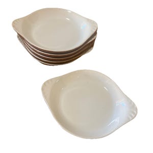 以下が含まれることがあります： 茶色の縁とスカラップエッジが付いた、6つの白い楕円形のセラミック皿のスタック。1つの皿が別々に表示されています。このお皿は、前菜や小分け料理を提供するのに適しています。