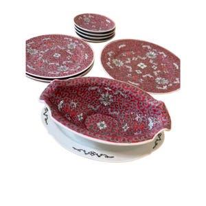 Puede incluir: Una colección de fuentes antiguas de porcelana roja y blanca. El juego incluye varios platos, fuentes ovaladas y una fuente para servir. Los platos presentan un estampado floral con detalles intrincados. La fuente para servir está sobre una base blanca.