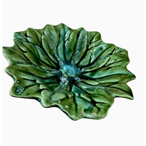 May include: A glossy, deep green ceramic dish shaped like a large, multi-petaled flower or a broad leaf. The surface features a vibrant, variegated glaze with darker green veins radiating from the center, which has a textured, blue-tinted finish.