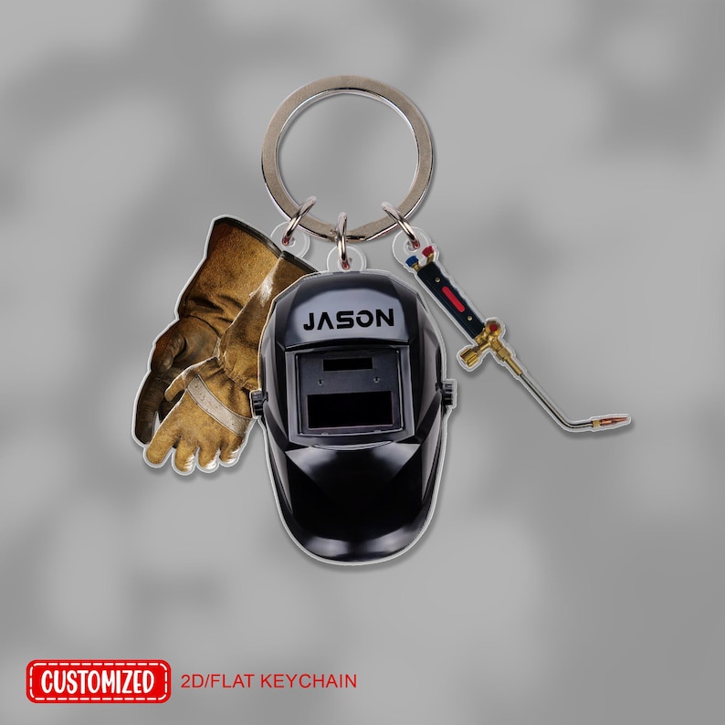 May include: A keychain featuring a black welding helmet with the name "JASON", brown work gloves, and a small torch. The keychain also has the text "CUSTOMIZED" and "2D/FLAT KEYCHAIN".
