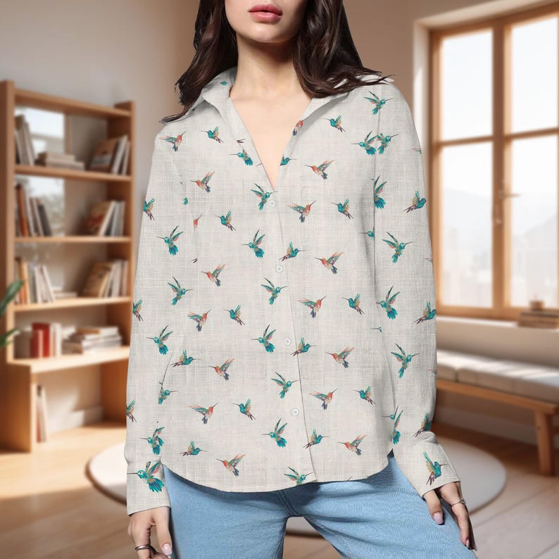 May include: A light-colored button-down shirt featuring a repeating pattern of hummingbirds in shades of teal, orange, and brown. The shirt has long sleeves and a classic collar. The background is a neutral color.