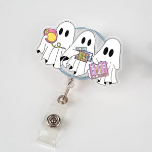 Può includere: Un portabadge con tre fantasmi dei cartoni animati. Ogni fantasma bianco ha occhi neri e tiene in mano un oggetto diverso: una radio rosa, una calcolatrice e una tavolozza di colori. Il portabadge ha un cinturino in plastica trasparente e una clip in metallo.