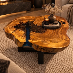 Peut inclure: Une table basse à bord naturel composée d'une dalle de bois avec une incrustation centrale en résine bleue. La table présente une finition polie, un grain de bois apparent et repose sur une structure de base en métal noir.