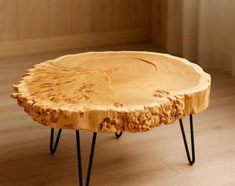 May include: A round, natural wood coffee table with a light brown finish. The table has a live edge and sits on three black hairpin legs. The table is approximately 30 inches in diameter.
