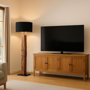 Pode incluir: Uma lumin&aacute;ria de ch&atilde;o com uma c&uacute;pula preta e interior dourado fica ao lado de um arm&aacute;rio de madeira com uma grande TV de tela plana. A lumin&aacute;ria tem uma base de madeira natural texturizada. O arm&aacute;rio &eacute; de madeira clara.