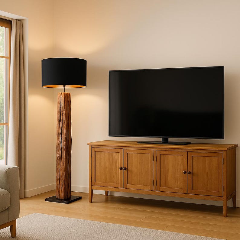 Pode incluir: Uma lumin&aacute;ria de ch&atilde;o com uma c&uacute;pula preta e interior dourado fica ao lado de um arm&aacute;rio de madeira com uma grande TV de tela plana. A lumin&aacute;ria tem uma base de madeira natural texturizada. O arm&aacute;rio &eacute; de madeira clara.