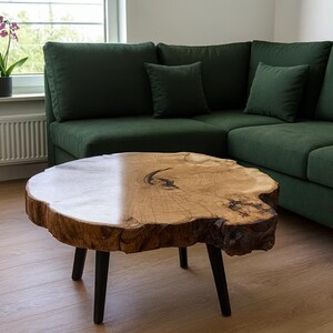 May include: A live-edge wooden coffee table with black legs sits in front of a dark green sectional sofa. The table has a natural wood grain finish and a unique, organic shape. The sofa has several throw pillows.