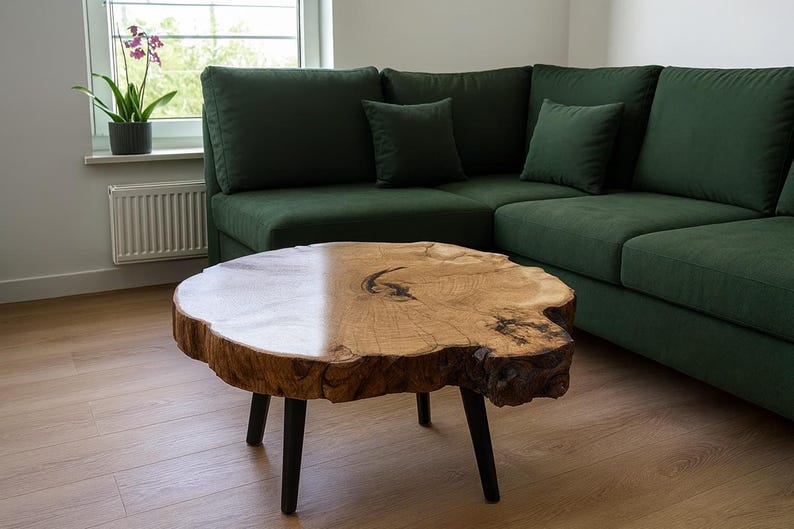 May include: A live-edge wooden coffee table with black legs sits in front of a dark green sectional sofa. The table has a natural wood grain finish and a unique, organic shape. The sofa has several throw pillows.