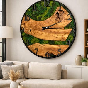 May include: A large, round wall clock with a black metal frame. The clock face features a natural wood design with a green moss background. Black numerals mark the hours. The clock hands are black.