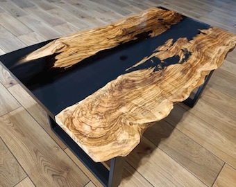 May include: A rectangular coffee table with a black glossy surface and a natural wood live edge. The wood has a light brown color with intricate grain patterns. The table is supported by a black metal frame.