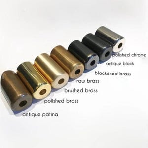 May include: An assortment of cylindrical metal objects in various finishes, including antique patina, polished brass, brushed brass, raw brass, blackened brass, antique black, and polished chrome. Each cylinder has a hole at one end. The objects are arranged diagonally.