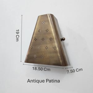 May include: Antique brass-colored wall sconce with a triangular shape, featuring decorative perforations. The sconce measures 7.50 cm deep, 18.50 cm wide, and 19 cm tall. The text "Antique Patina" is visible at the bottom.