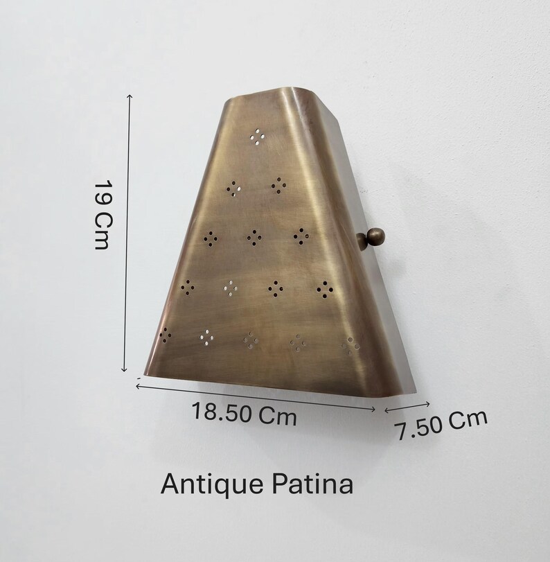 May include: Antique brass-colored wall sconce with a triangular shape, featuring decorative perforations. The sconce measures 7.50 cm deep, 18.50 cm wide, and 19 cm tall. The text "Antique Patina" is visible at the bottom.