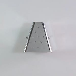May include: A trapezoidal, polished chrome metal tea infuser featuring a hinged design with a small spherical knob on each side. The surface is perforated with a repeating pattern of small, four-dot floral-like clusters across the front face.
