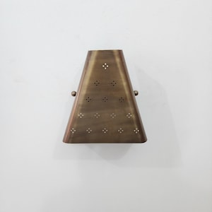 “Handmade vintage brass wall sconce front view, trapezoid metal shade with small perforated cutout pattern, antique brass finish wall light on white background.”