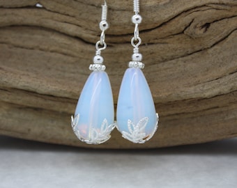 Può includere: Un paio di orecchini a goccia d'argento con pietre di opale bianco. Gli orecchini hanno un delicato design a filigrana attorno alle pietre.