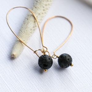 May include: A pair of gold hoop earrings with black lava rock beads. The earrings are simple and elegant, perfect for everyday wear.