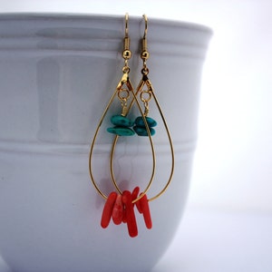 May include: Gold teardrop earrings with turquoise and coral stones. The earrings are dangling from a white surface.
