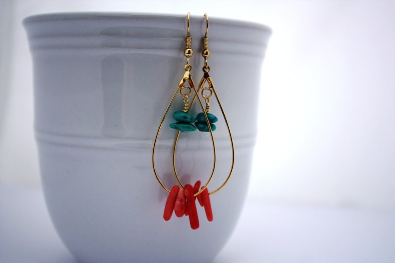 May include: Gold teardrop earrings with turquoise and coral stones. The earrings are dangling from a white surface.