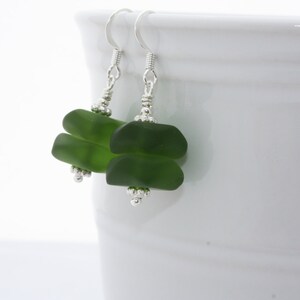 May include: A pair of green glass earrings with silver hooks and beads. The earrings are made of two stacked pieces of green glass.