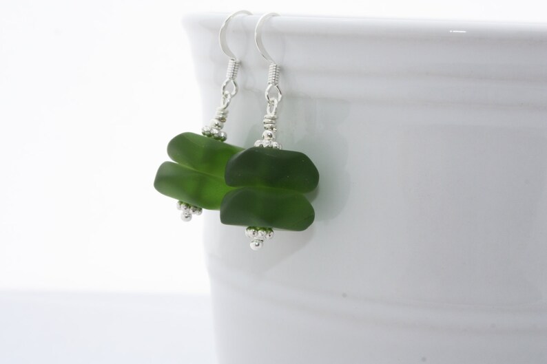 May include: A pair of green glass earrings with silver hooks and beads. The earrings are made of two stacked pieces of green glass.