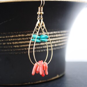 May include: Gold teardrop earrings with turquoise and coral beads. The earrings are hanging from a black surface.