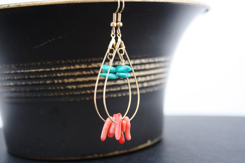 May include: Gold teardrop earrings with turquoise and coral beads. The earrings are hanging from a black surface.