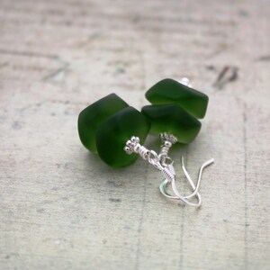 May include: A pair of earrings with green glass beads and silver wire accents.