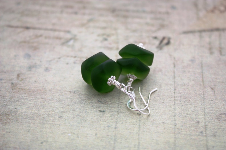 May include: A pair of earrings with green glass beads and silver wire accents.