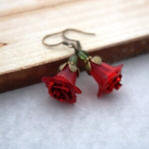 May include: A pair of red rose earrings with green accents. The earrings are made of glass and have a bell shape.