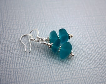 May include: Teal blue glass bead earrings with silver hooks and silver beads. The earrings are made with three beads each.