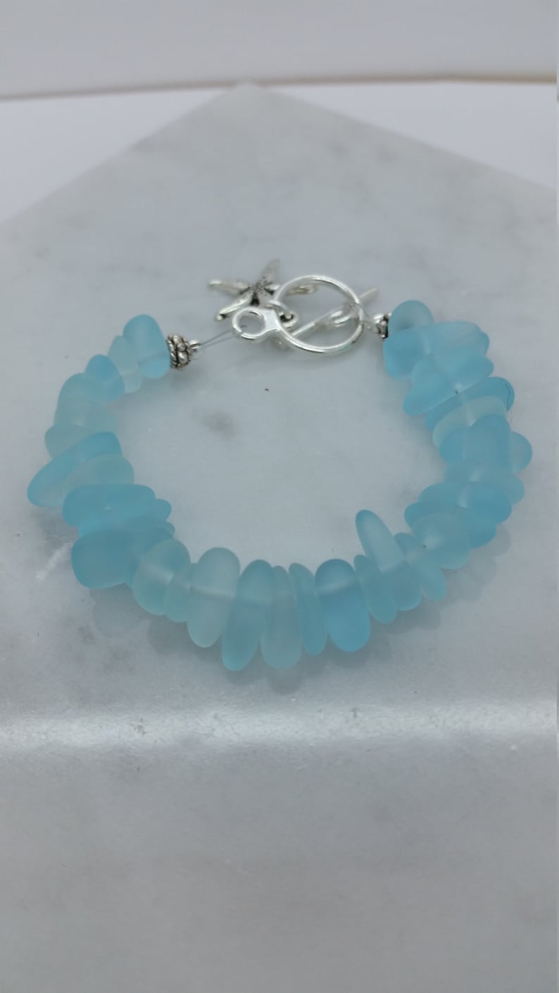 Pu&ograve; includere: Un braccialetto in vetro di mare blu chiaro con una chiusura argentata. Il braccialetto &egrave; fatto di pezzi lisci e arrotondati di vetro di mare.