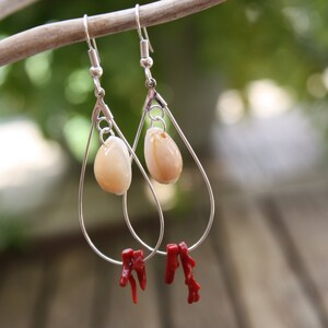 May include: Silver teardrop earrings with a white shell charm and red coral accents.