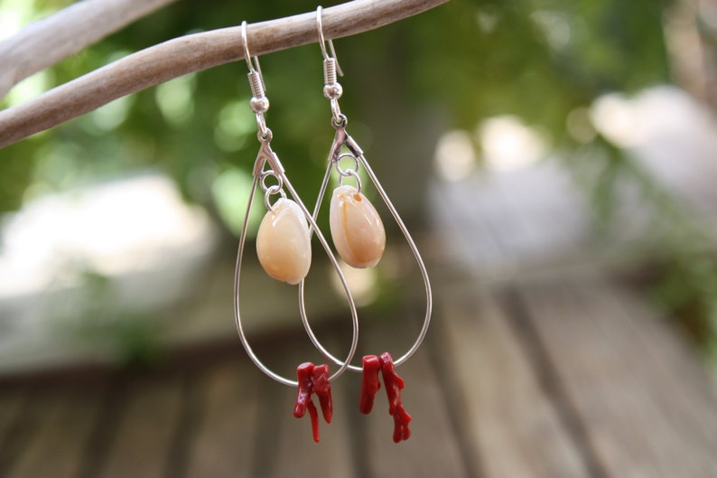 May include: Silver teardrop earrings with a white shell charm and red coral accents.