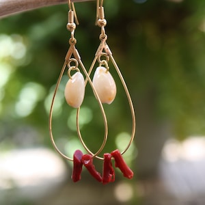 May include: Gold teardrop earrings with a white shell charm and red coral accents.
