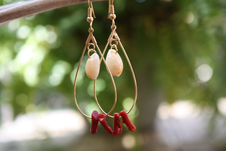 May include: Gold teardrop earrings with a white shell charm and red coral accents.