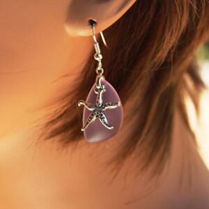 Puede incluir: Pendientes de vidrio de mar morado con un dije de estrella de mar plateado.