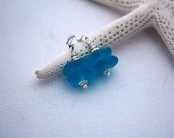 May include: A pair of turquoise blue sea glass earrings with silver wire and beads. The earrings are hanging from a starfish.