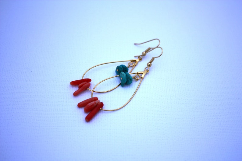 May include: Gold dangle earrings with turquoise and coral accents. The earrings feature a teardrop shape with a small loop at the top for hanging.