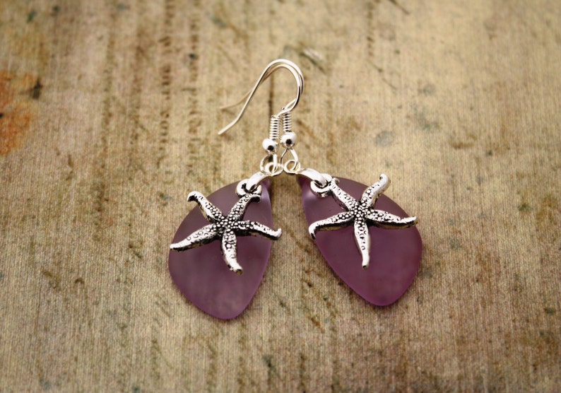 Puede incluir: Pendientes de vidrio morado con dijes de estrella de mar plateados. Los pendientes tienen forma de l&aacute;grima y est&aacute;n suspendidos de ganchos plateados.