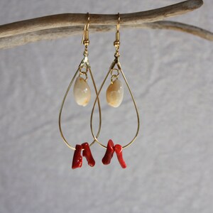 May include: Gold teardrop earrings with a white shell charm and red coral accents.