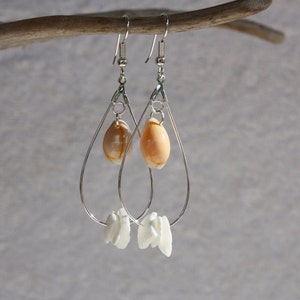 May include: Silver dangle earrings with a teardrop shape. The earrings feature a small seashell charm and a larger seashell charm.
