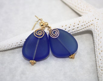 May include: A pair of blue glass earrings with gold wire spirals. The earrings are teardrop shaped and have a frosted finish.