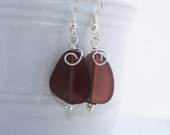 May include: A pair of earrings with a dark purple teardrop-shaped glass bead and a silver wire swirl. The earrings are attached to silver hooks.