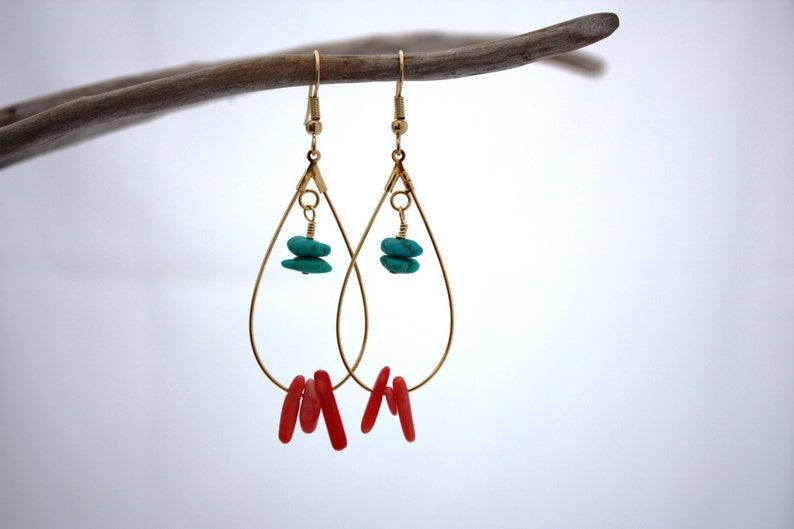 May include: Gold teardrop earrings with turquoise and coral accents. The earrings are hanging from a branch.