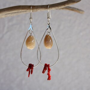 May include: Silver teardrop earrings with a beige shell charm and a red coral dangle.