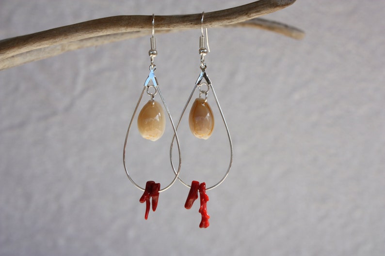 May include: Silver teardrop earrings with a beige shell charm and a red coral dangle.