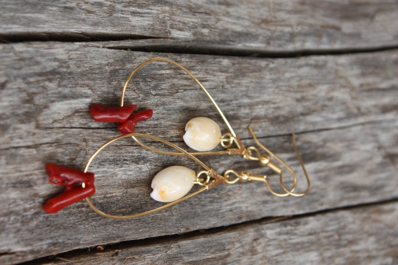 May include: Gold hoop earrings with a white shell charm and a red coral charm hanging from each hoop.