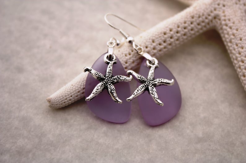 Puede incluir: Un par de pendientes de plata con colgantes de l&aacute;grima de vidrio morado y abalorios de estrella de mar plateados.