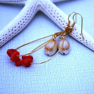 May include: Gold dangle earrings with red coral beads and white shell accents.